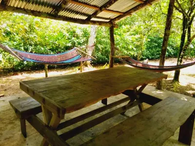two hammocks and a wooden table and bench under a roof at Nacientes Lodge in Bijagua