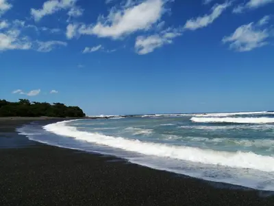 a black beach with waves crashing on the shore at Contenedor Santa Cruz en Guanacaste piscina in Paraíso