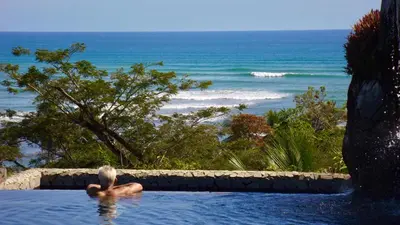 a man in a swimming pool looking at the ocean at Casa Vista Pacifico in Esterillos