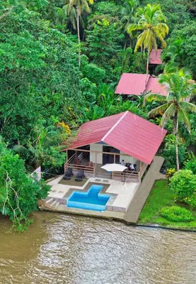 a house with a red roof next to a river at Valverde Glamping & Ecolodge in Tortuguero