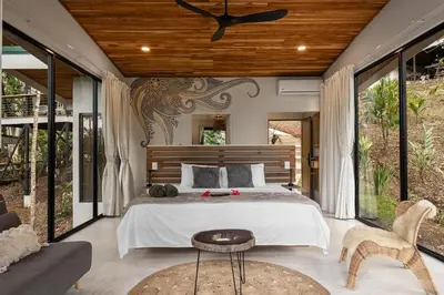 a bedroom with a bed and a couch and windows at Pandanus Lodge & Retreats Bungalow Heliconia in Cariblanco