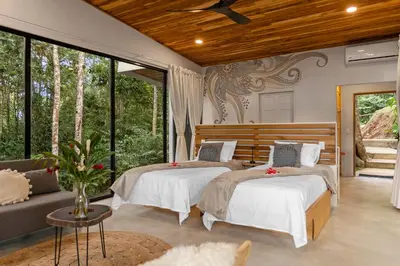 a bedroom with two beds and a couch and windows at Pandanus Lodge & Retreats Bungalow Heliconia in Cariblanco