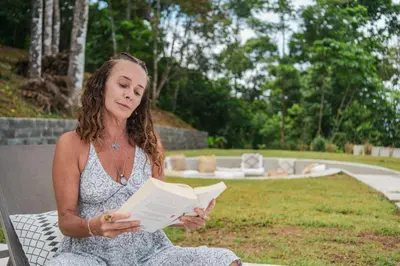 a woman sitting on a bench reading a book at Pandanus Lodge & Retreats Bungalow Heliconia in Cariblanco