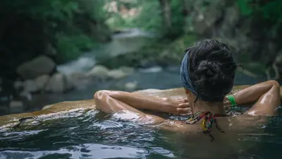 a woman sitting in the water in a river at Pandanus Lodge & Retreats Bungalow Heliconia in Cariblanco