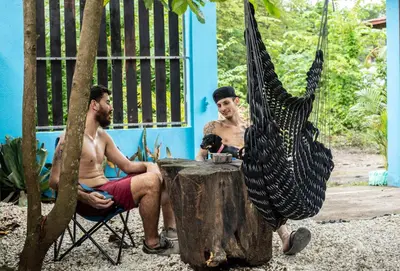 two men sitting at a table next to a tree stump at Argdivan Beach Hostel in Sámara