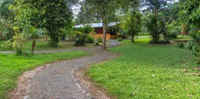 a path through a park with a house in the background at Hacienda el Paraíso in Guápiles