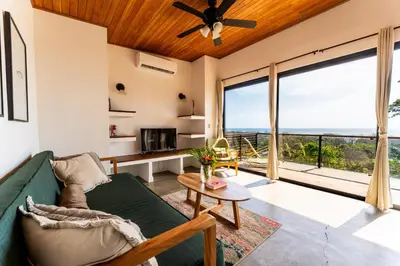 a living room with a green couch and a large window at Ocean Apartments- Walk to the beach in Santa Teresa Beach