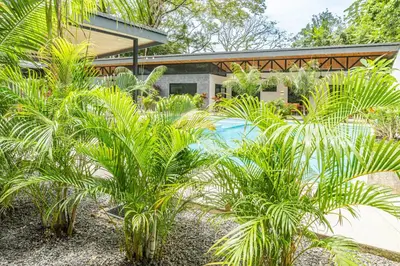 a garden with palm trees in front of a house at Coco Nosara Villas Guiones Family Resort Casa Lluvia in Nicoya