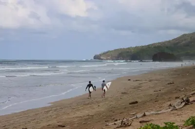 two surfers walking on the beach with their surfboards at Steps to the Main Surf Break - Casita 1 Dos Hijas in Refundores