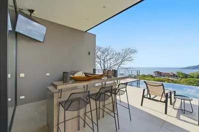 a kitchen with a bar with chairs and a pool at Amazing Ocean and Mountain Views in Tamarindo