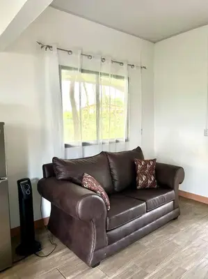 a brown leather couch in a living room with a window at Miravalles Tiny House in Upala