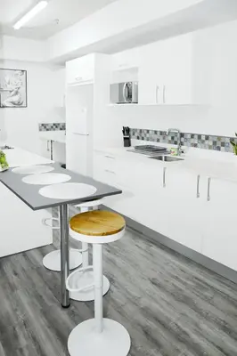 a white kitchen with white cabinets and a wooden stool at Grotto at 28, City Views and Wonderland Vibes! in Hatillo