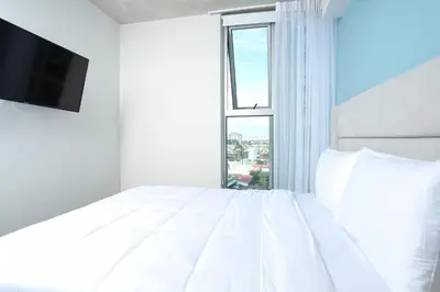 a white bedroom with a large white bed and a window at Teal at 12, City Views and Wonderland Vibes! in Hatillo