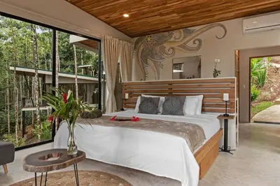 a bedroom with a large bed and large windows at Pandanus Lodge & Retreats Bungalow Strelizia in San Ramón