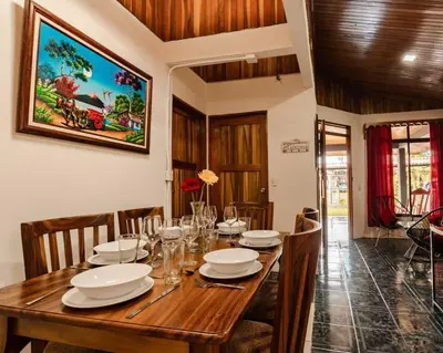 a wooden dining room table with plates and glasses on it at Gaby's Home In Downtown La Fortuna in Fortuna