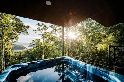 a swimming pool in the middle of a forest with the sun shining at Arenal Summit in Nuevo Arenal
