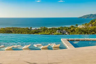a pool with chairs and the ocean in the background at Wyndham Tamarindo in Tamarindo