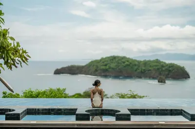a woman sitting on the edge of a pool looking out at the ocean at Nekajui Peninsula Papagayo, a Ritz-Carlton Reserve in Papagayo, Guanacaste