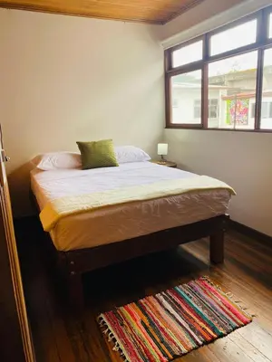 a bed in a bedroom with a window and a rug at Casa 1856- cómodas habitaciones en el Centro de Alajuela in Alajuela City