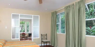 a bedroom with a bed and a chair and windows at Airport Costa Rica B&B in Alajuela City