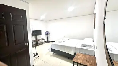 a white bedroom with a bed and a television at Marianas Apartments 5MIN SJO AIRPORT in Alajuela City