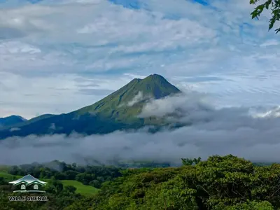 a mountain in the clouds with a house in the foreground at Valle Arenal in Fortuna