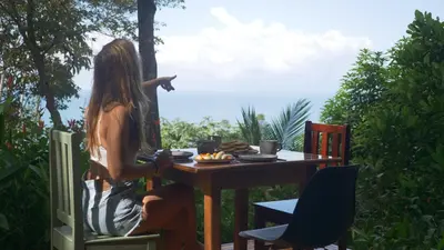 a woman sitting at a table pointing at the ocean at Casa Oh - Oceanview Guesthouse in Uvita