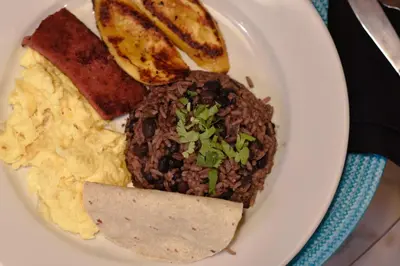a plate of food with rice and beans and bread at Brisas del Aeropuerto Airport Breezes inn in Heredia