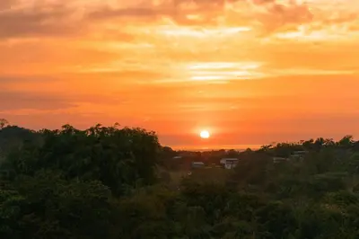 a sunset with the sun in the sky over trees at Tardes Doradas in Quepos