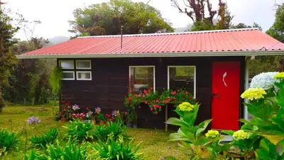 a small house with a red door and flowers at Finca La Picuda Quetzal Cottage in Cartago