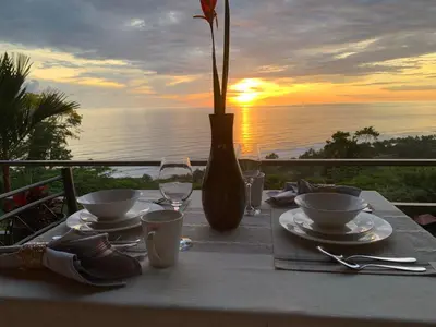 a table with plates and cups and a vase with the sunset at Villa Del Mar 3 Spectacular ocean view in Savegre