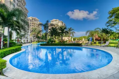 a swimming pool at a resort with palm trees and buildings at Primium Jaco Bay in Jacó