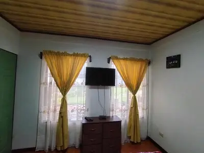 a living room with yellow curtains and a television at Hospedaje con relajante Vista in Grecia