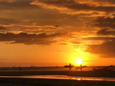 two people walking on the beach with their surfboards at sunset at Tsunami Hostel in Tamarindo