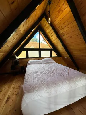 a bed in a attic with a large window at Cabaña La Trinidad de Dota in El Copey