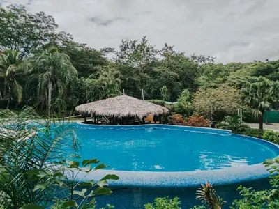 a large blue swimming pool with a thatch hut at Beautiful Condo, Tamarindo Costa Rica in Huacas