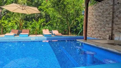 a swimming pool with chairs and an umbrella at Jardín de los Monos in Matapalo
