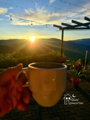 a person holding a coffee cup with the sunset in the background at Glamping Los tucanes in San José