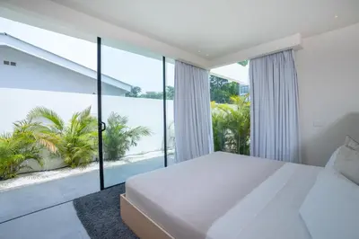 a bedroom with a white bed and large windows at Villa Juba Tamarindo Centro in Tamarindo