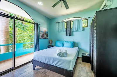 a bedroom with a bed with blue walls and a window at Casa Mariposa in Jacó