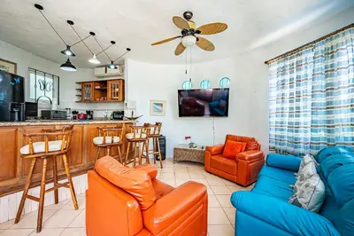 a living room with orange furniture and a kitchen at Casa Mariposa in Jacó