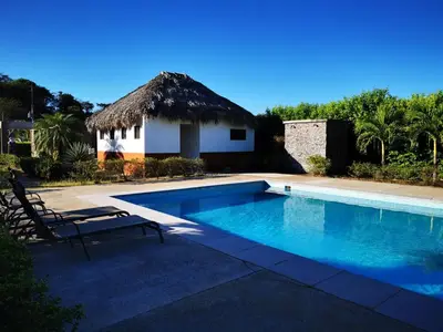 a swimming pool in front of a house with a thatch roof at Casa Lucas in Villarreal