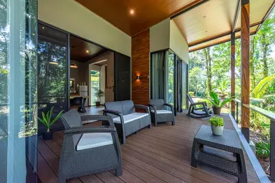 a screened porch with wicker chairs and tables at Río Sarapiquí Lodge in Sarapiquí