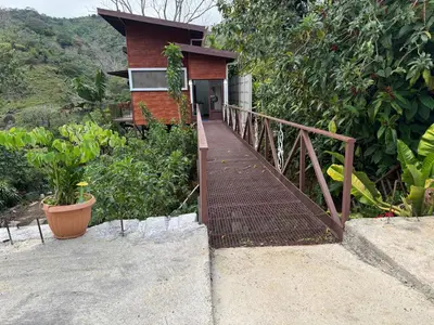 a wooden bridge leading to a house with trees at Cabaña Lotf Atenas in San Isidro