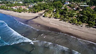 an aerial view of a beach with people in the water at Beach Break Resort & CR Surf Camp in Jacó