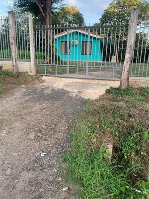 a fence with a blue house behind a tree at Hospedaje Oropendola Nest in Bagaces