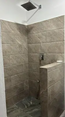 a bathroom with a shower with a stone wall at Alojamiento Coral in Quepos