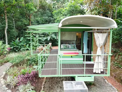 a tiny house with a porch in a garden at Jungle Bus, 5 min drive to PlayaLinda, 15 to Dominical, Wifi Starlink in Quepos