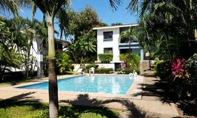 a swimming pool in front of a house with palm trees at Minimalist Condo with a Beautiful New Design, Bound Patio, and Shared Community Pool in Coco