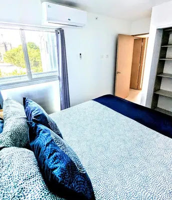 a bed with blue pillows in a room with a window at Modern Paradise Relax & Explore at Viva Jaco in Jacó